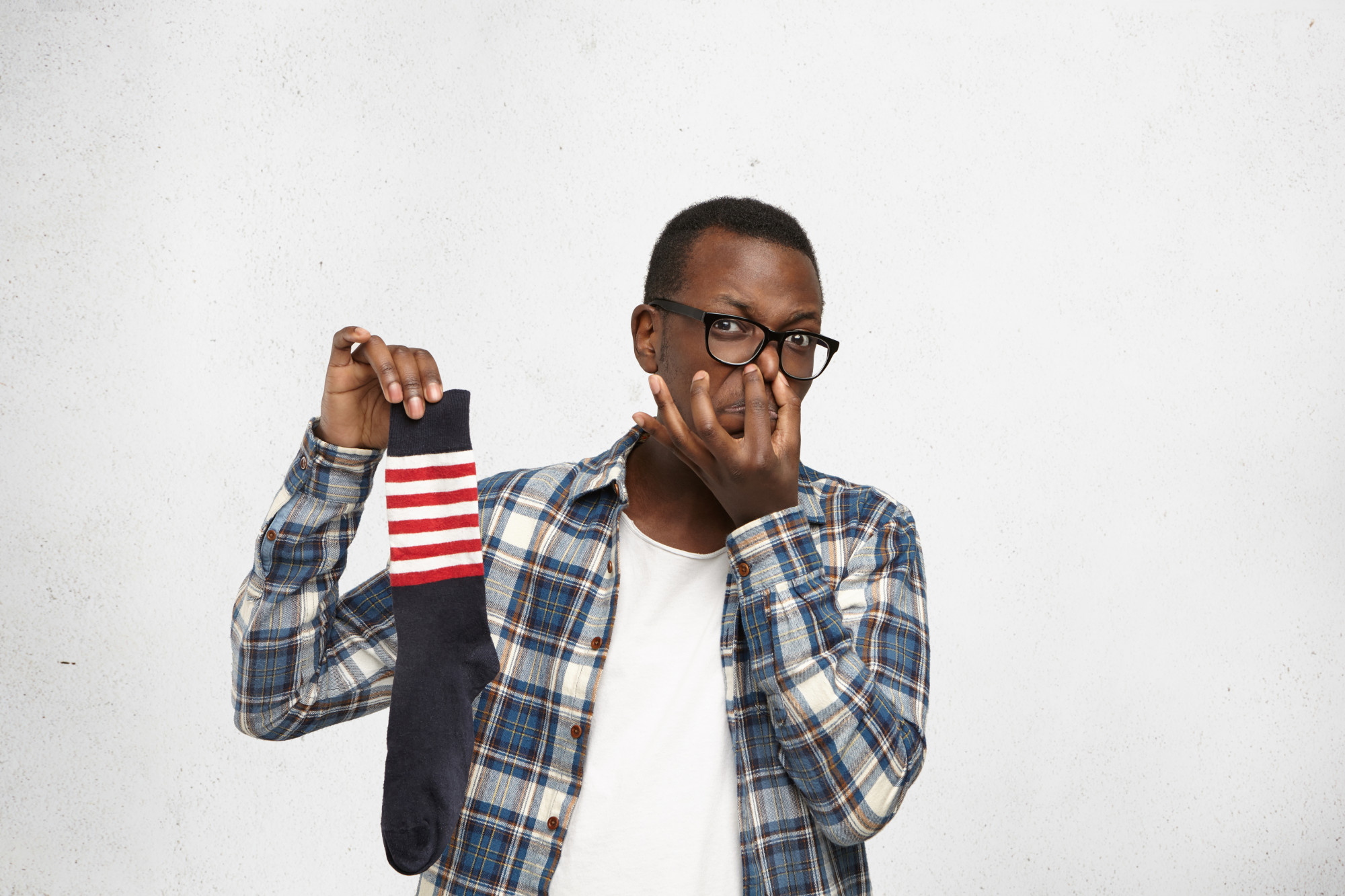 man with glasses holding up sock in one hand, holding nose in other hand