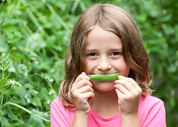 Young girl eating peas from a vegetable garden