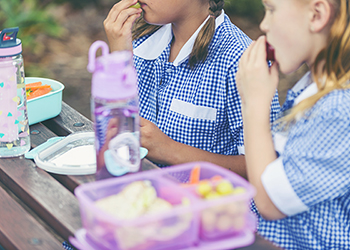 Two schoolgirls eating lunch from lunchboxes