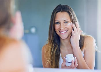 young lady looking at reflection while applying moisturiser to her cheek
