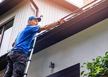 Man standing on a ladder cleaning the gutters