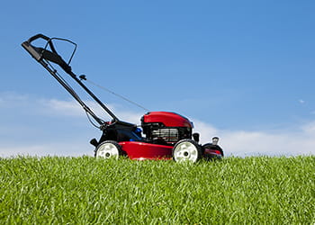 Red lawnmower on green grass against a blue sky