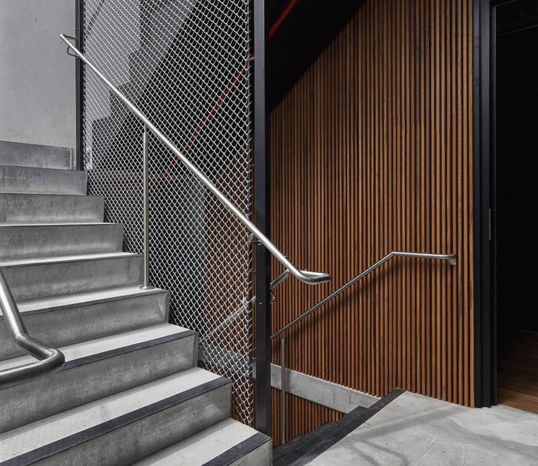Staircase with concrete steps, timber slat walls and wire mesh.
