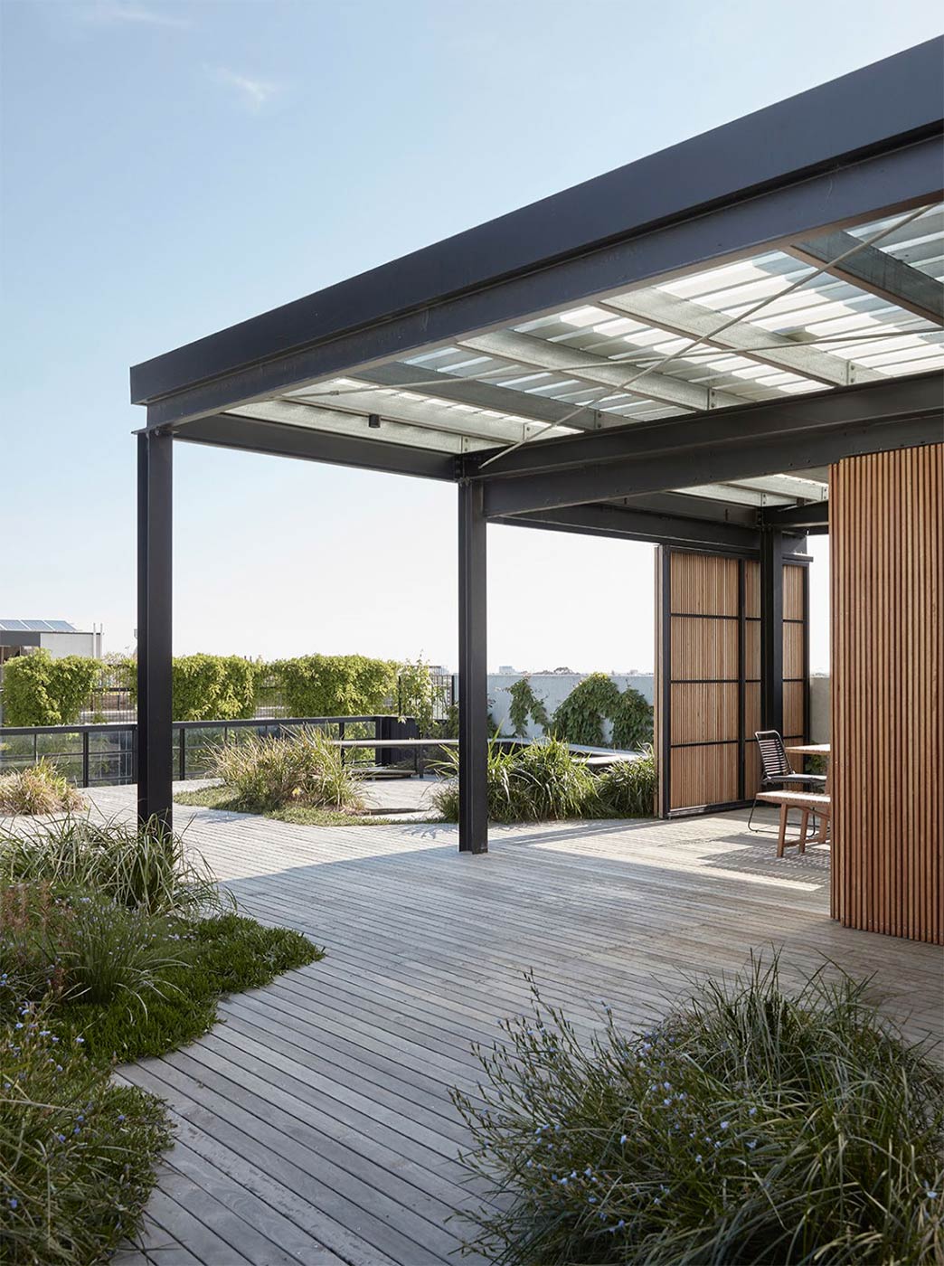 A building’s rooftop with a metal structure to provide shelter, timber decking and grassy landscaping.
