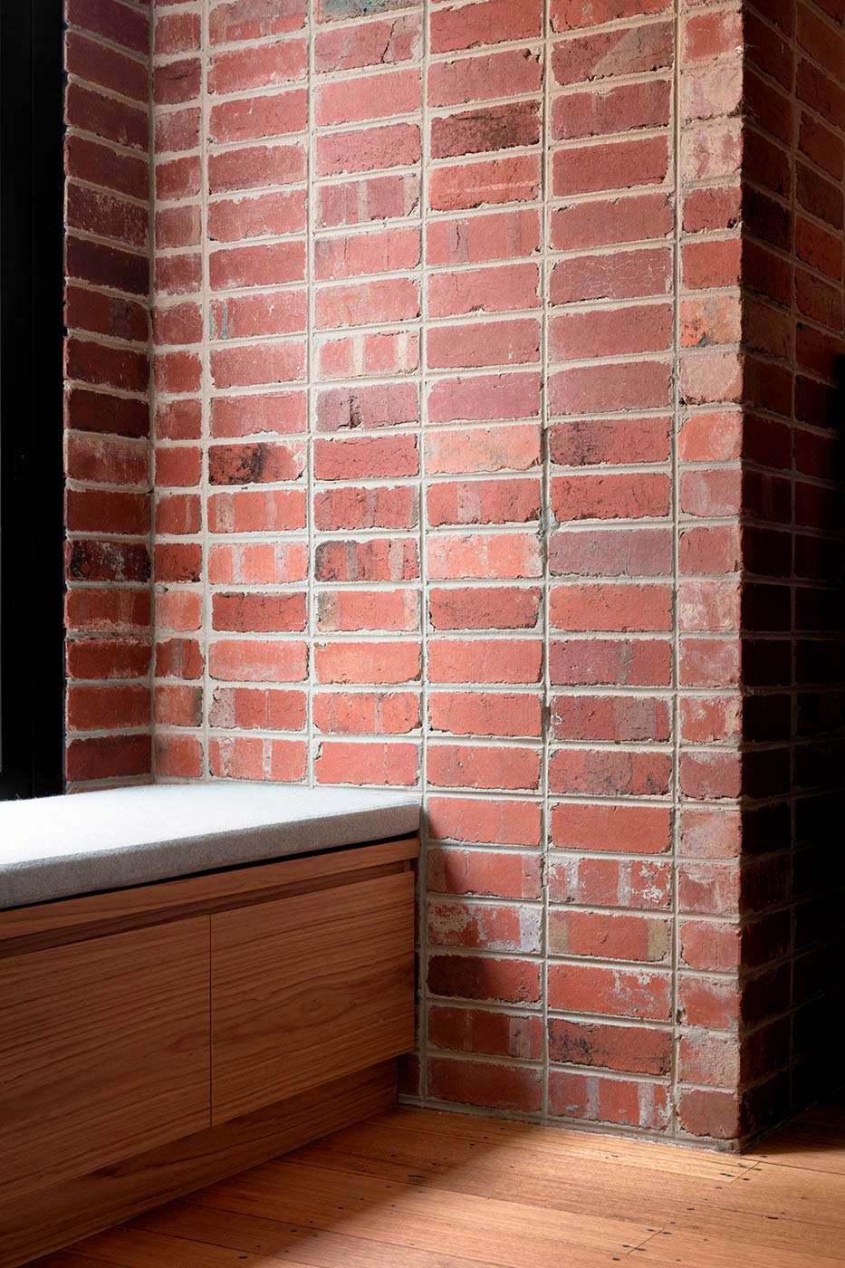 Brick wall with upholstered seating near window. Joinery below.