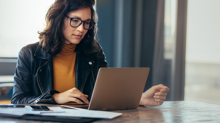 A woman sits at a desk and stares at her laptop screen.