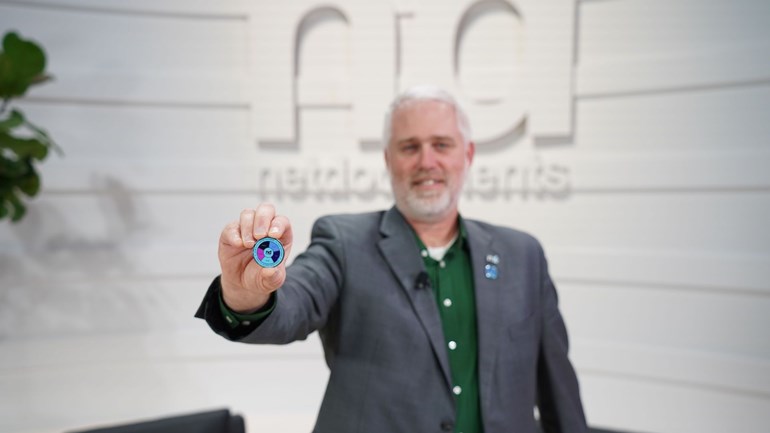 NetDocuments' Mike Sanders holds the NetDocuments Solution Wheel as a coin in his hands while smiling at the camera.