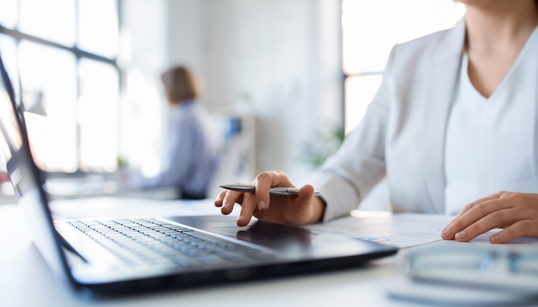 Primer plano de una mujer sentada en su escritorio mientras está en una computadora portátil.