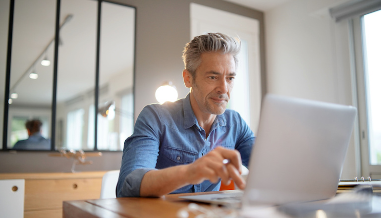 Um homem está sentado em uma mesa sorrindo para uma tela de computador.