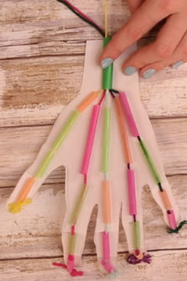 A hand-shaped piece of paper with small pieces of drinking straws taped to it. There is string threaded through the paper.