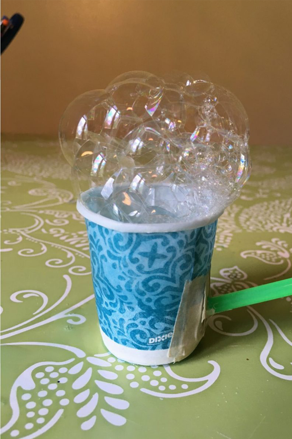 A paper cup with a straw taped to it and bubbles flowing out of if.