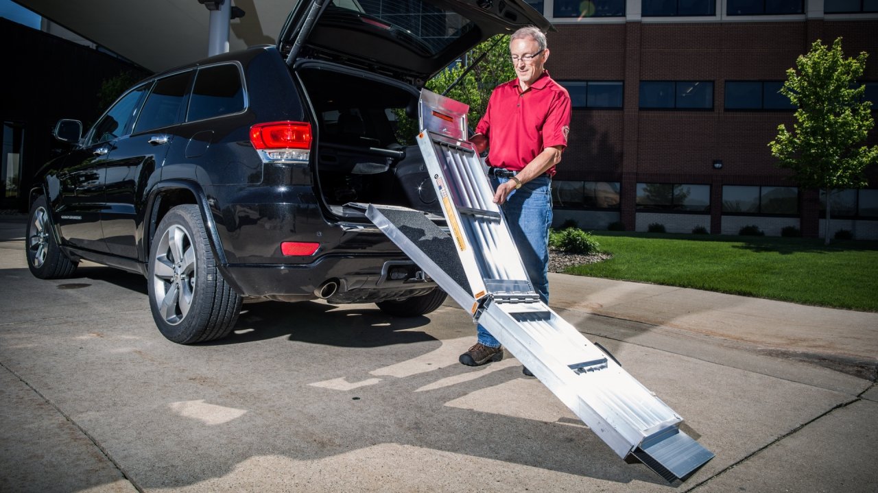 Man folding the EZ Access Trifold Ramp outside a SUV's tailgate.