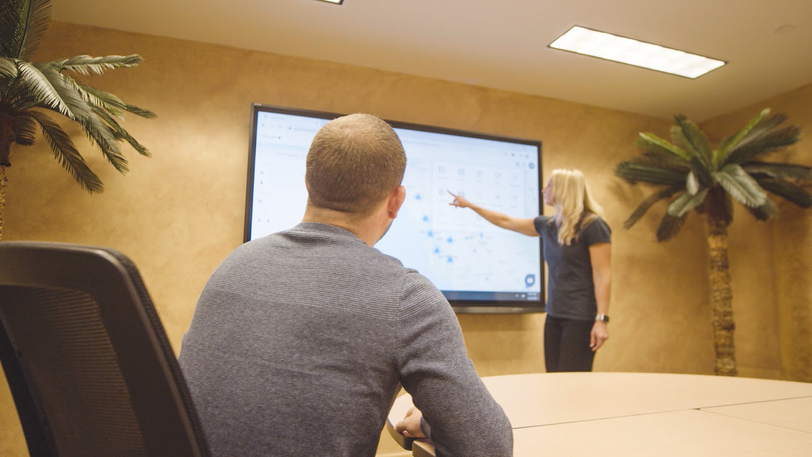 Woman demonstrates how to use a software on a touchscreen television to a man.