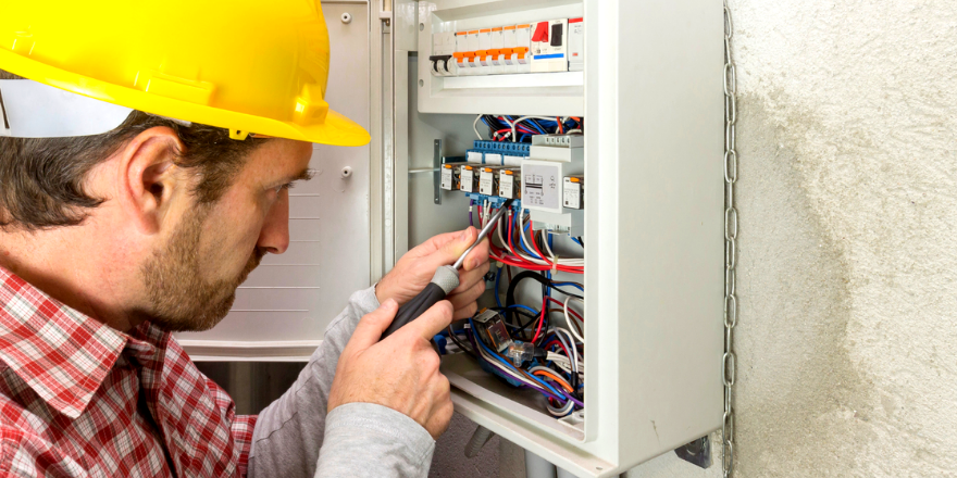 A man in a hardhat works on an electrical box.