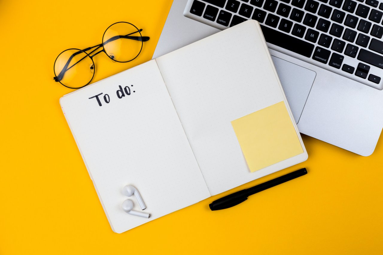 A to-do list, glasses and laptop on a yellow background.