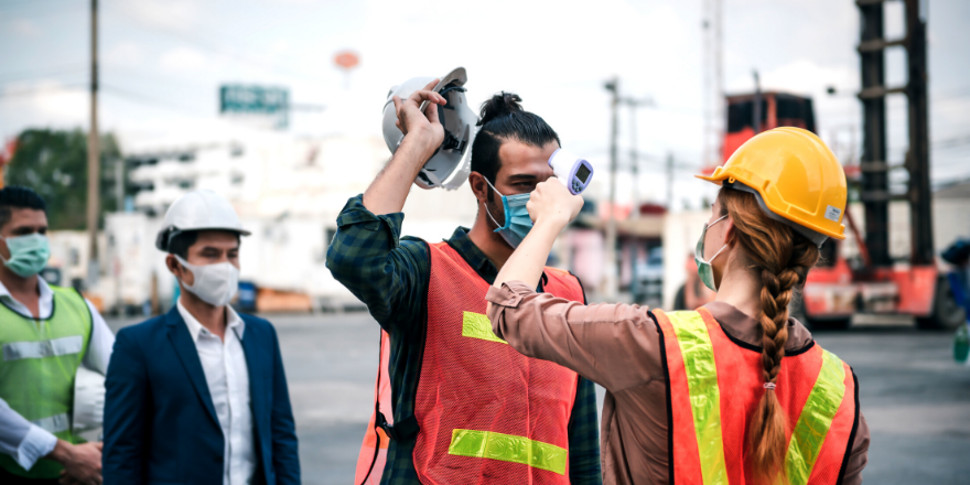 A woman construction worker taking the tempature of other construction workers.