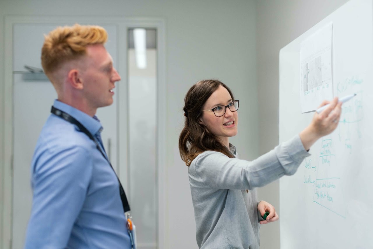 A woman draws a picture on a whiteboard to demonstrate an idea to a male coworker.