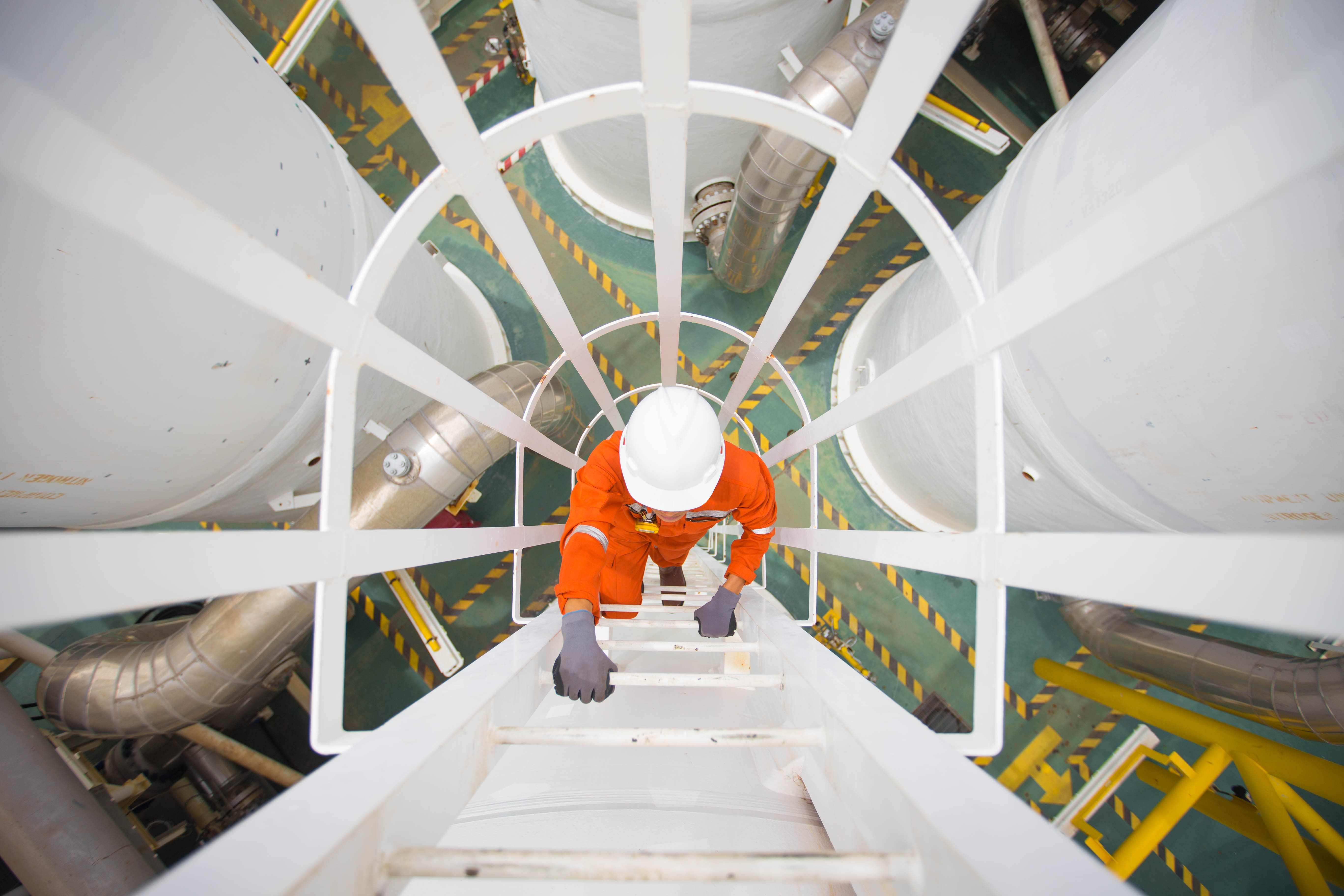 An above view of a worker climbing a white ladder at a mechanical construction site.
