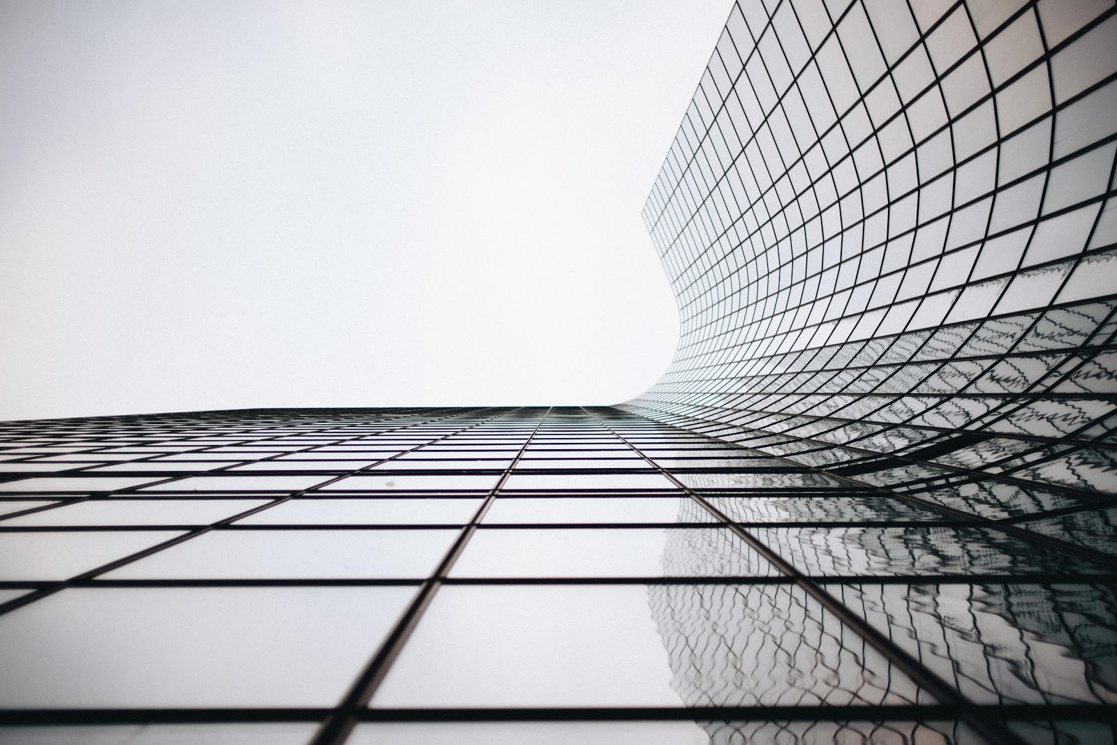 A curved glass building with a reflection of another building.