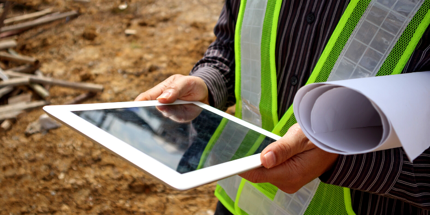 A construction worker holding a white tablet and blueprints