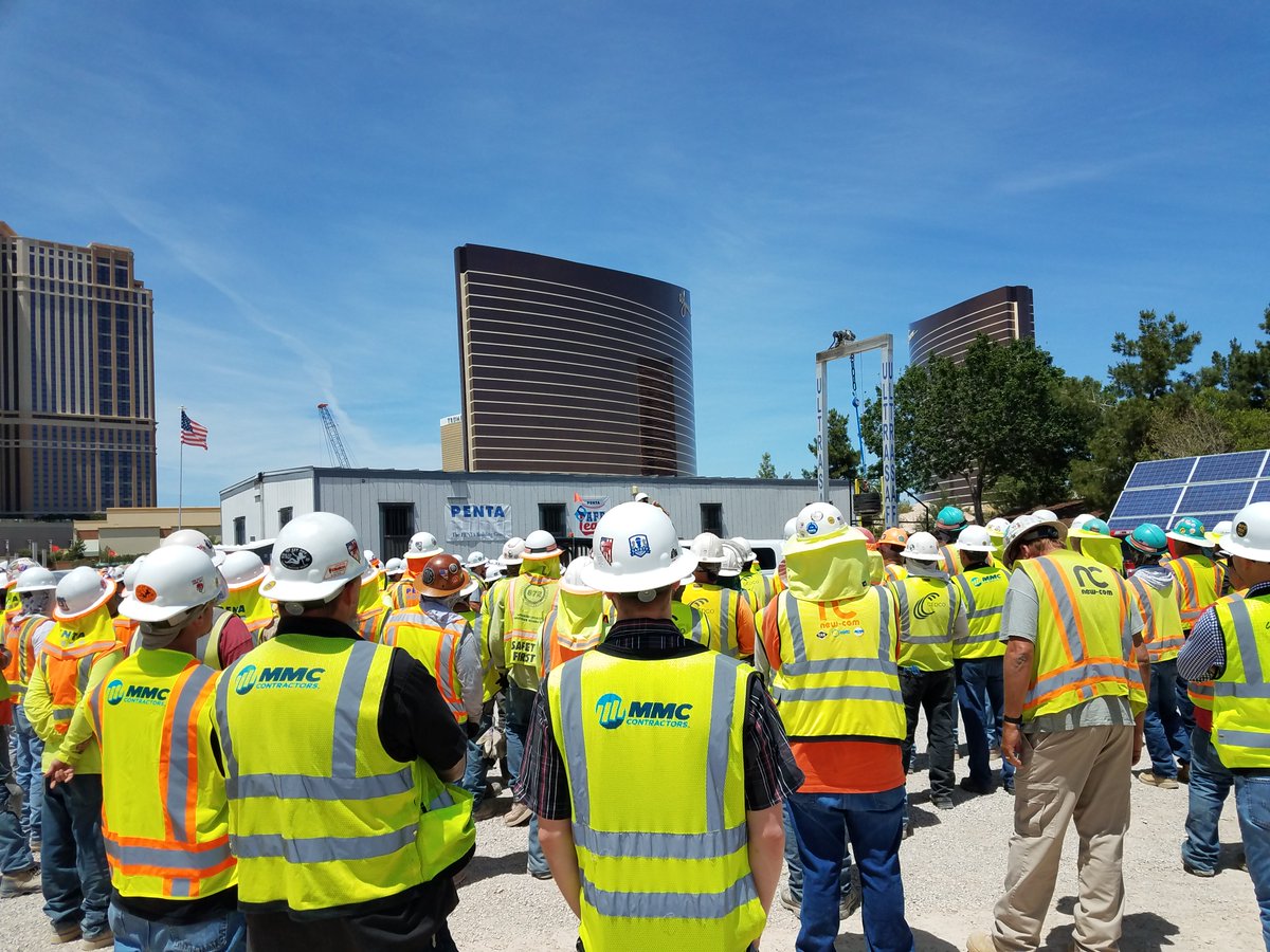 A group of mechanical construction workers huddled around a trailer at a building site.