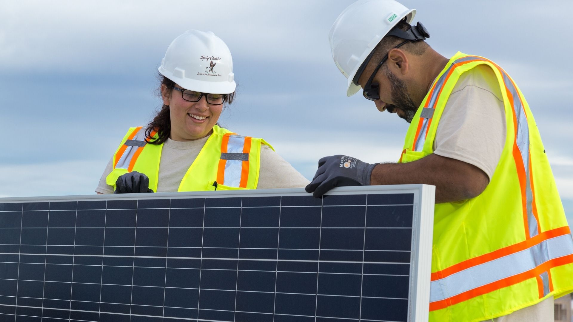 Two Sprig Electric construction workers working together on a solar panel.