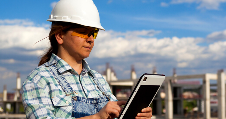A woman construction worker on a tablet looking out in the distance.