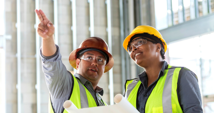 Two construction workers pointing and looking out at something behind the camera.