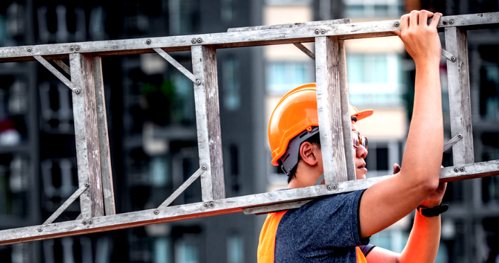 A male construction worker carrying a ladder.