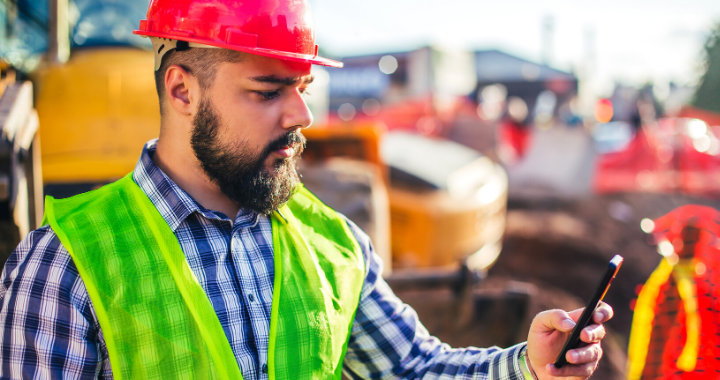 A construction worker looking at his phone on a jobsite.