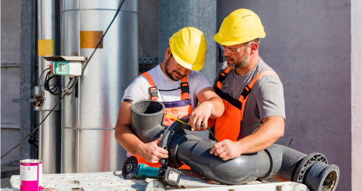 Two plumbing-specific construction workers attaching two pipes.
