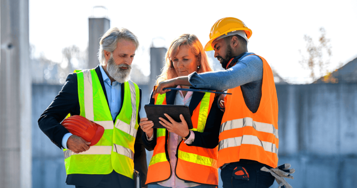 Two male and one female construction workers in safety gear observing a workforce management platform on the iPad.