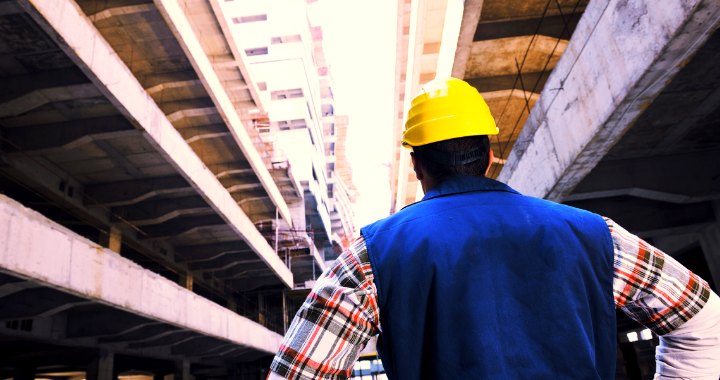 A male construction worker underneath construction, looking out into the distance.