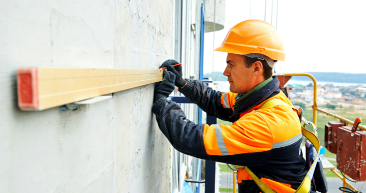 Male construction worker marking the level point on a building with a level.
