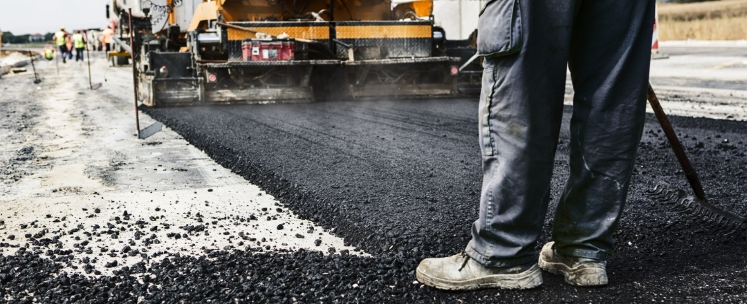 Man's legs on newly laid asphalt during road construction.