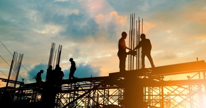 Six construction laborers work on a metal structure at sunset.