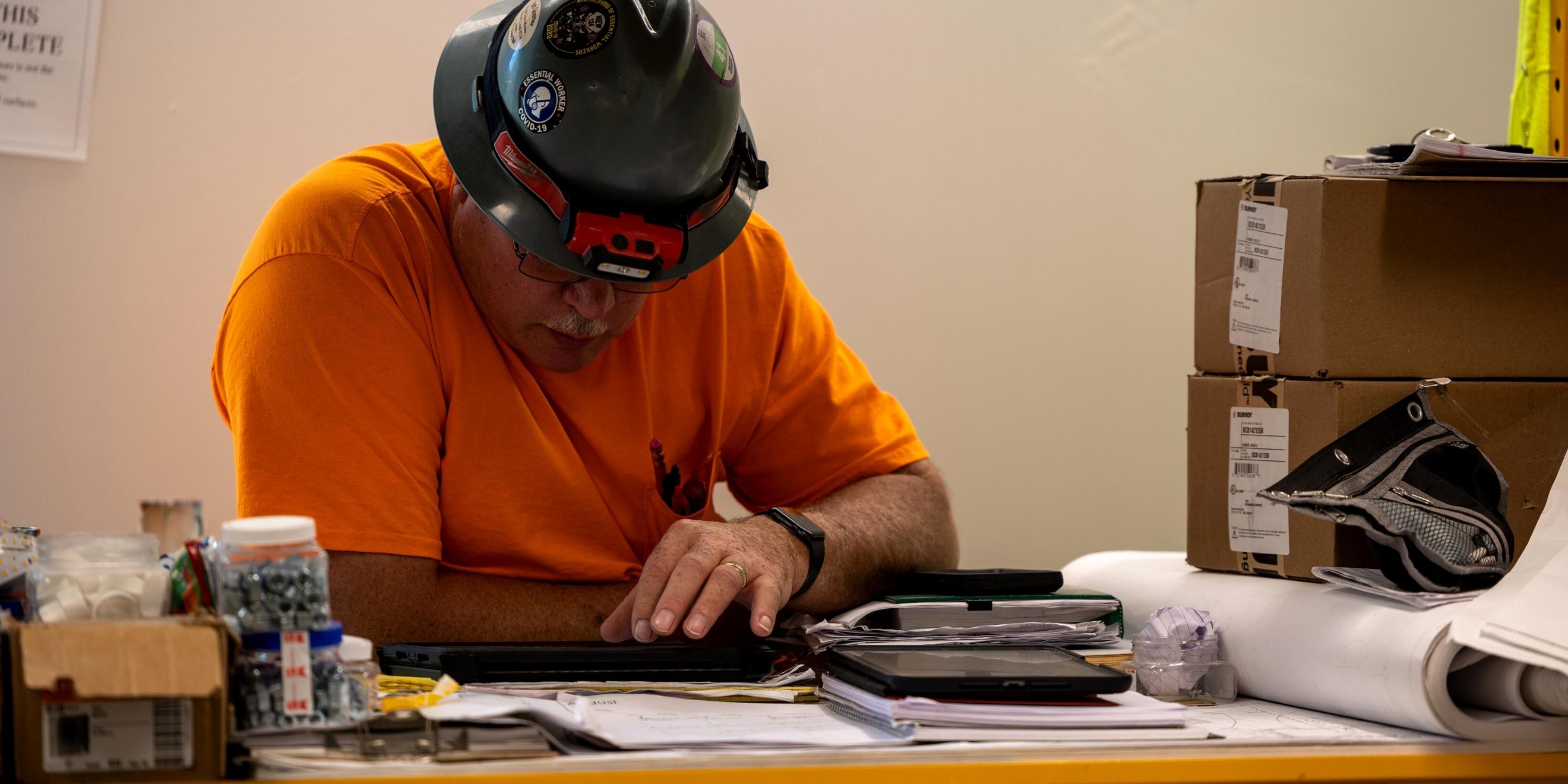 A construction worker in a jobsite trailer communicates with his team via a tablet.