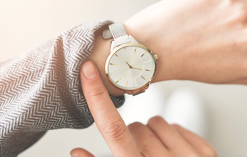 Close-up of a wristwatch on a person's arm. They're pulling back their shirt sleeve to expose the watch face.