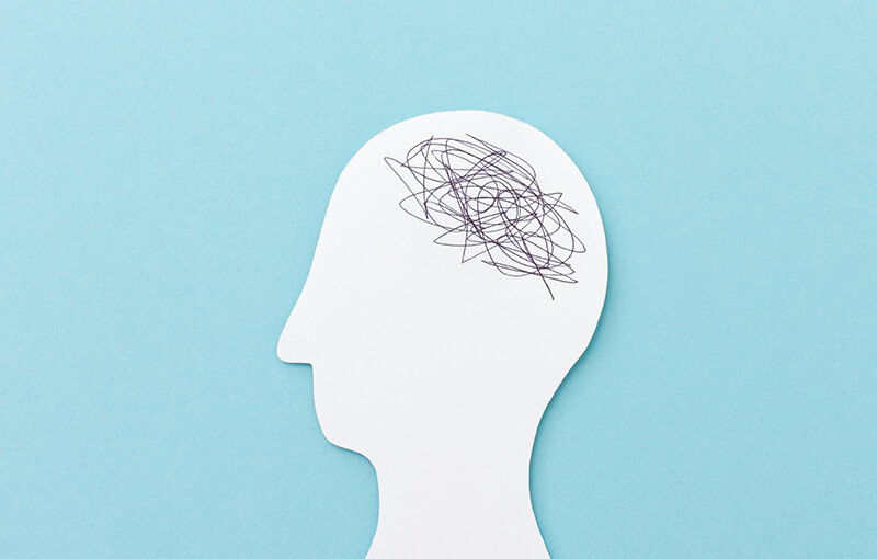 Paper cut out of the shape of a person's profile with the area where the brain would be covered in black scribbles.