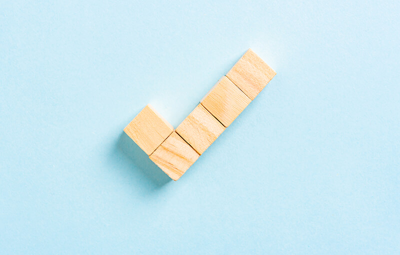 A checkmark made out of 5 wooden cubes.