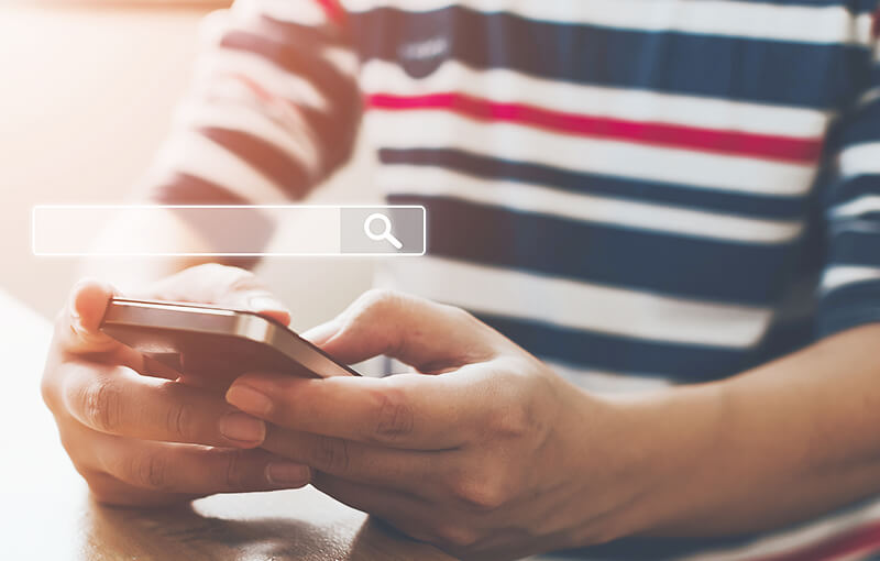 Close-up of a man's hands holding a mobile phone. Above the phone is a floating search bar.