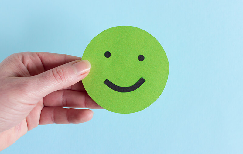 A hand holding a green paper circle with a happy face drawn on it.