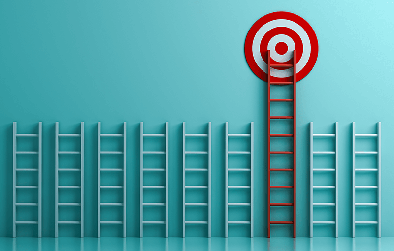 A line of 9 white ladders leaning against a light aqua wall. The seventh ladder is taller than the others and colored red, and at the top of it is a red and white target.