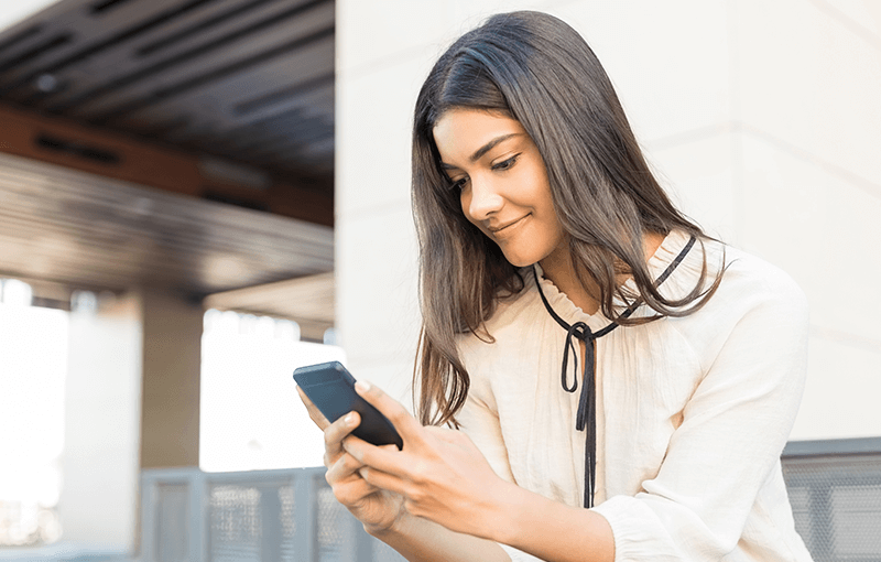 Young woman sits on steps, holding and looking at her mobile phone - Neovation Learning Solutions