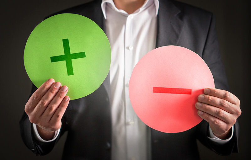 A person holding up two circles; one is green with a "plus" sign and one is red with a "minus" sign - Neovation Learning Solutions