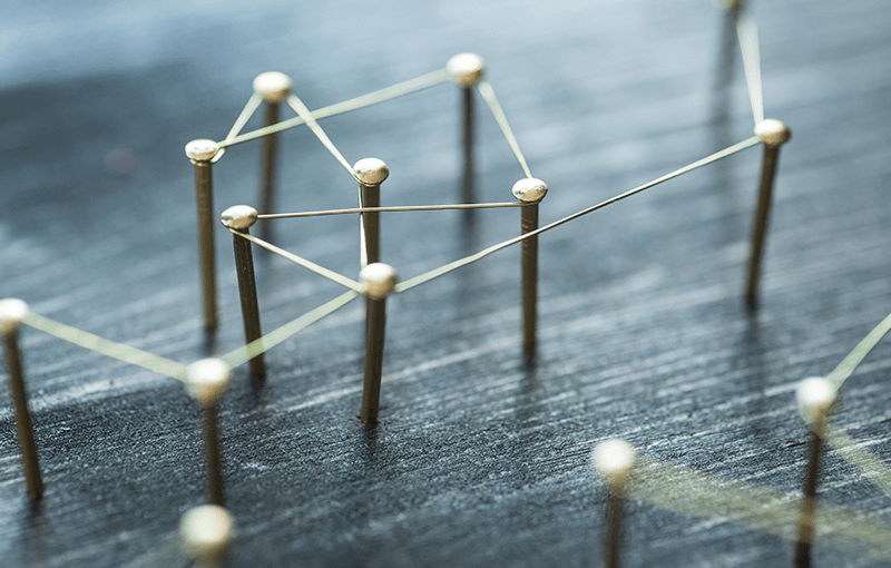 Image depicts a series of nails hammered into a board with a pieces of string connecting each of them randomly. - Neovation Learning Solutions