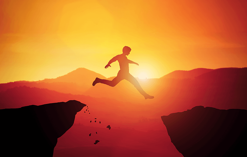 Image of a silhouetted figure jumping off a cliff across a gap to another cliff, against a sunset - Neovation Learning Solutions