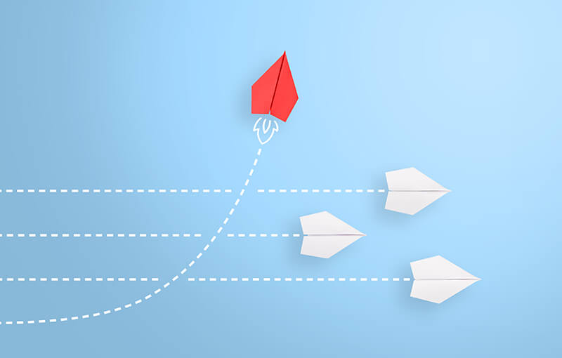 Three white paper airplanes flying in a straight line to the right. One red paper airplane turns and intersects the lines of the white paper planes and continues going up.