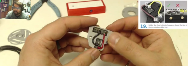 A screenshot showing the build of the accessible switches. In the top-right corner is the How-to step photo; in the top left is a man in goggles. The main screen shows a close-up of hands holding the small mechanical parts of a switch.