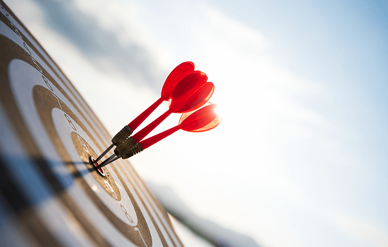 Three red darts in the center of a target, against a blue sky.